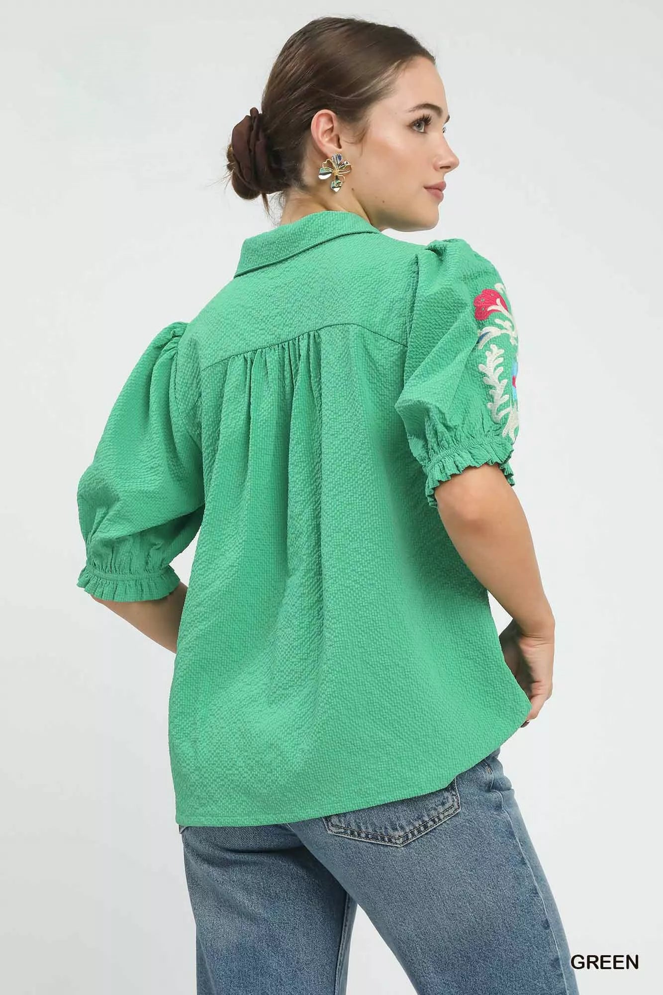Close up of green seersucker fabric with floral embroidery on short sleeves