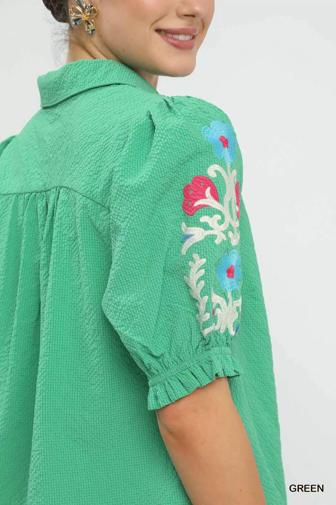 Close up of green seersucker fabric with floral embroidery on short sleeves