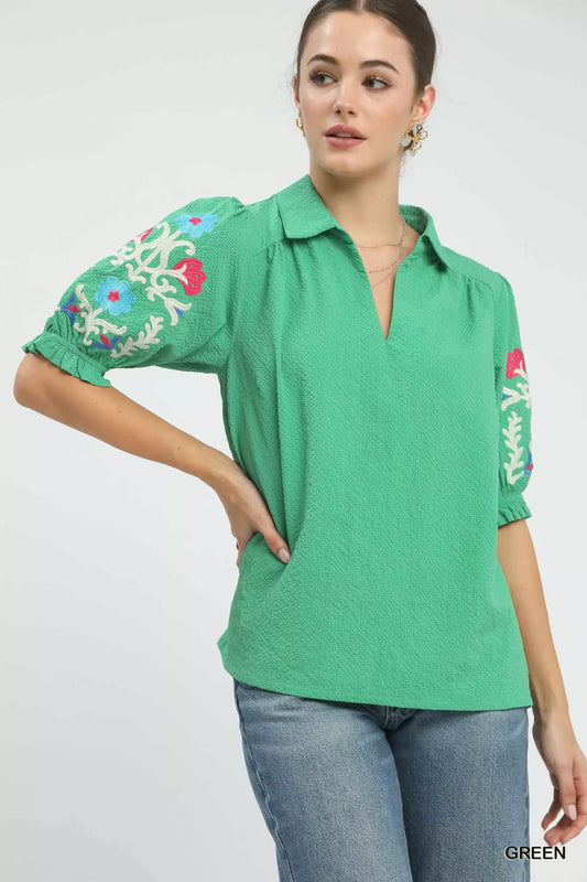Close up of green seersucker fabric with floral embroidery on short sleeves